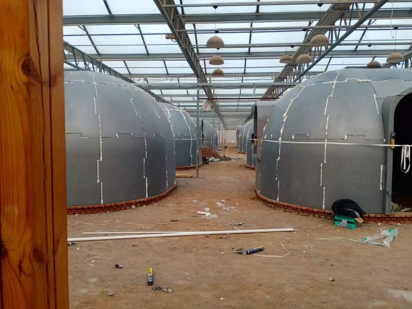 Rows of dome-shaped metal structures inside a greenhouse, construction in progress.