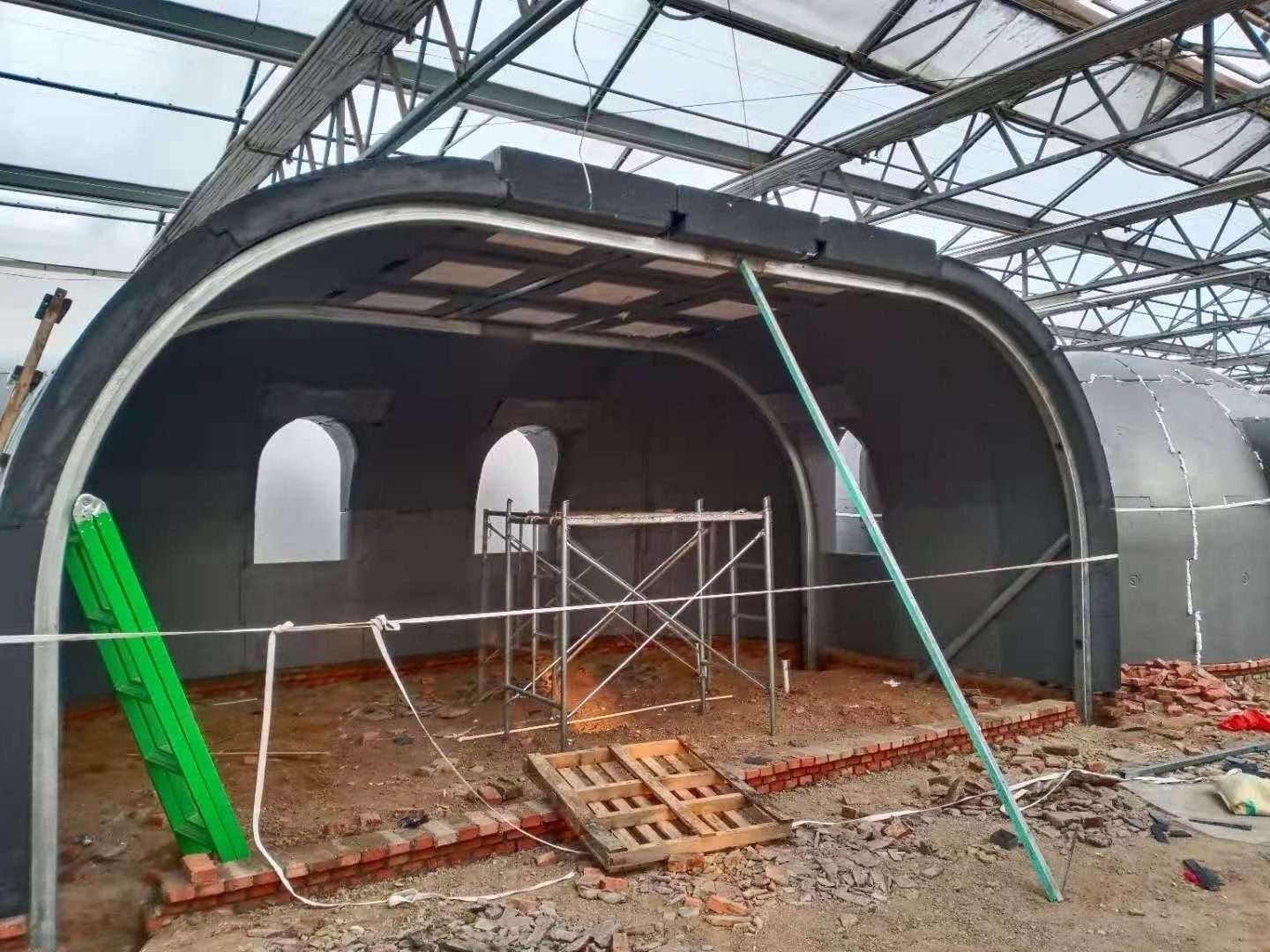Construction of a dark gray, arched structure; scaffolding and bricks visible inside.