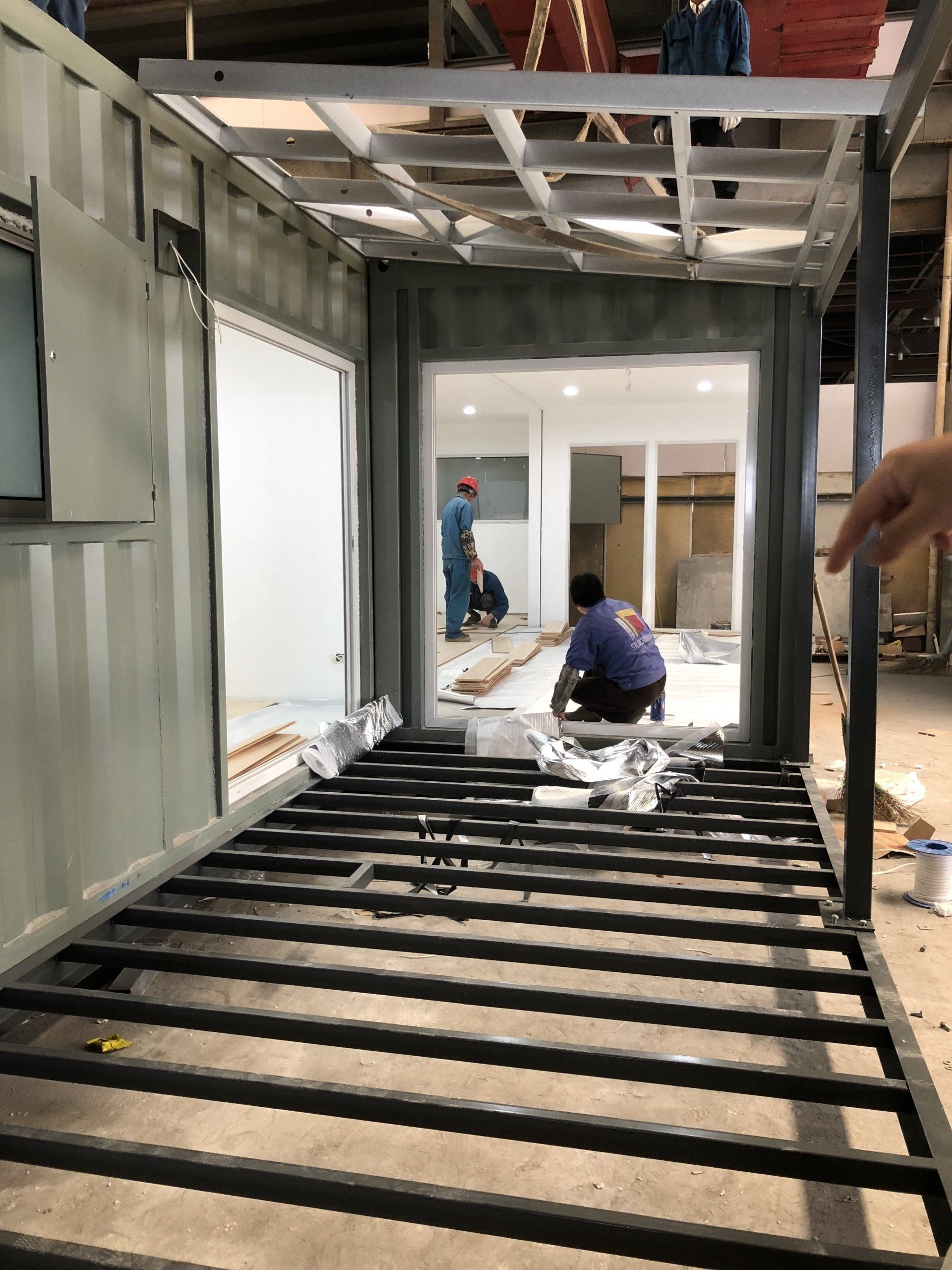 Interior of a container building under construction, workers inside, metal frame, open doorway.