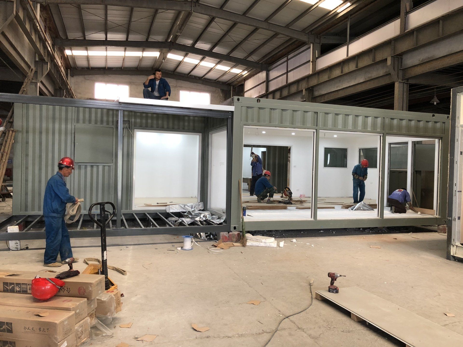 Workers constructing modular building from shipping containers inside a large warehouse.