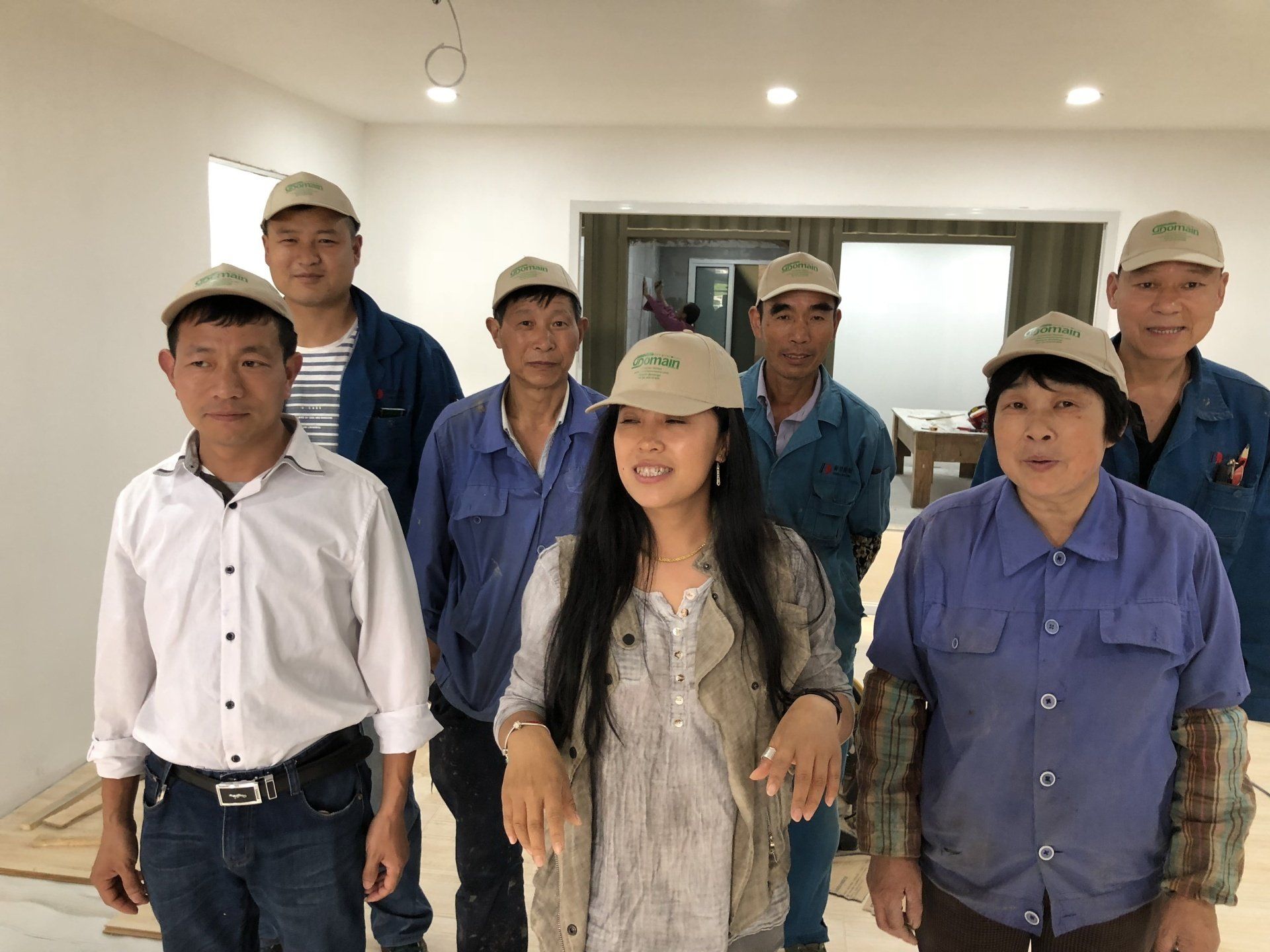 Group of seven people wearing caps, standing in a room. Some are in work uniforms, smiling.