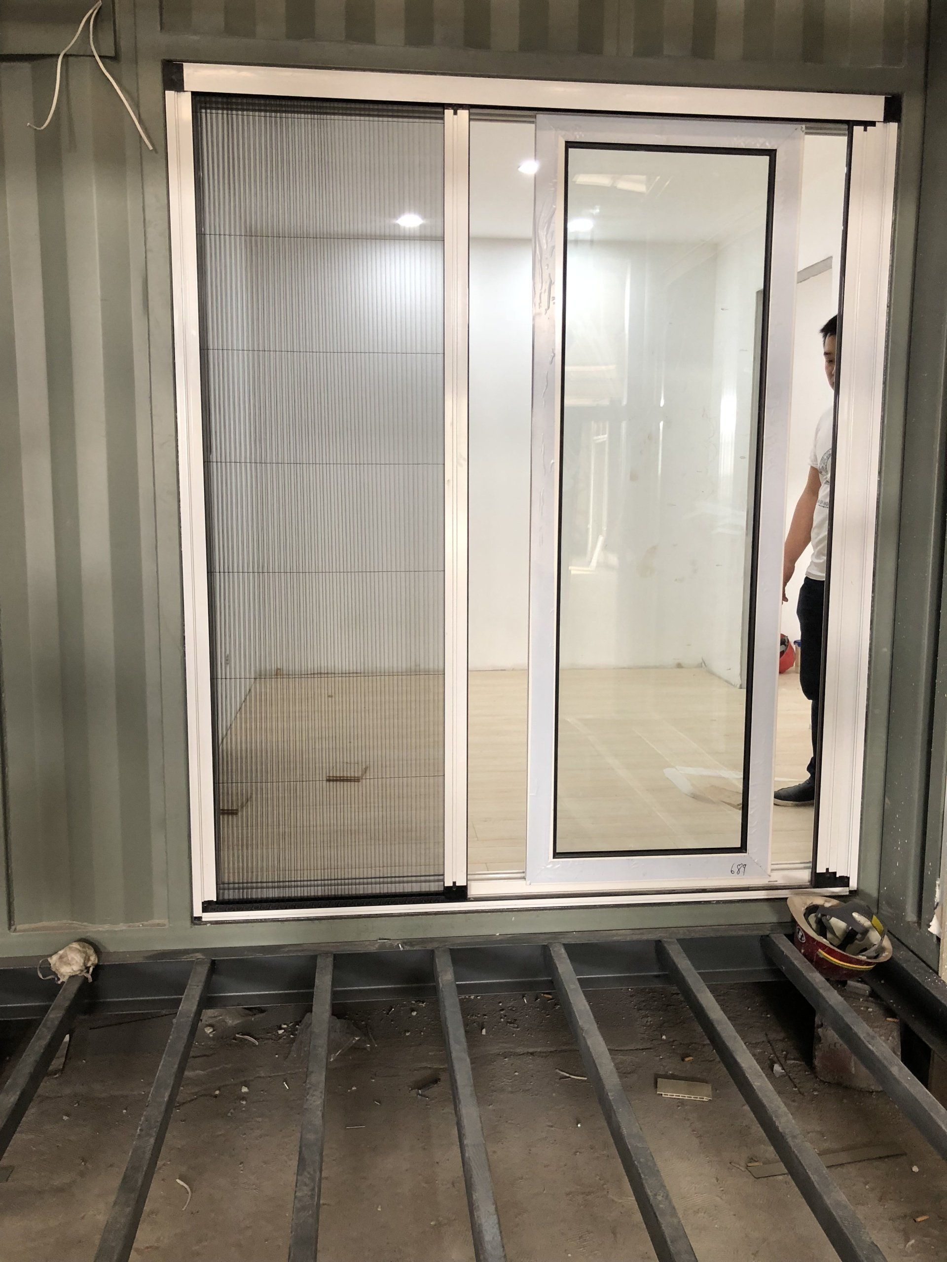 Sliding glass door with screen in a container, person visible, unfinished floor.