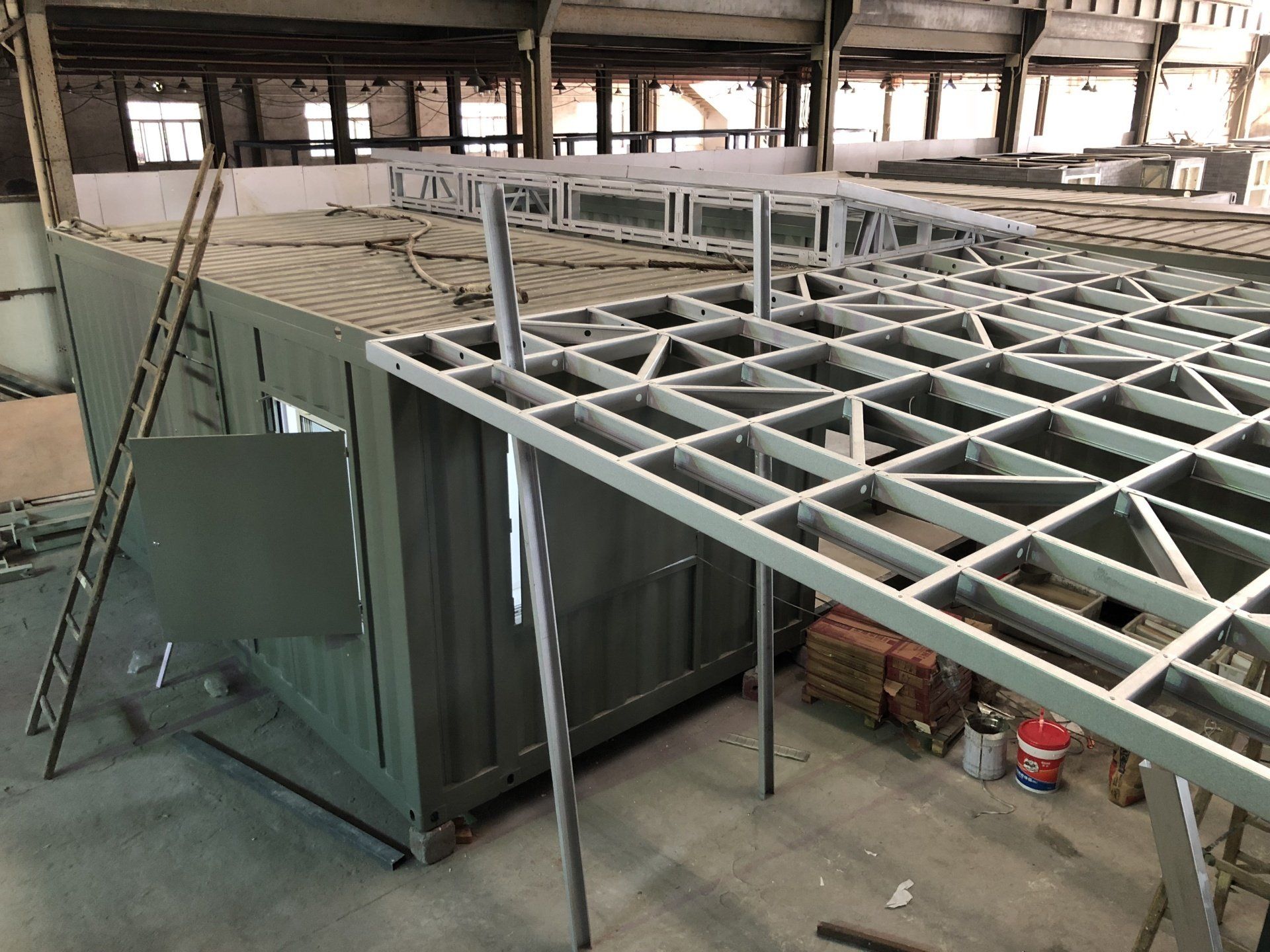 Construction site with metal frame structure being built onto a green container building.