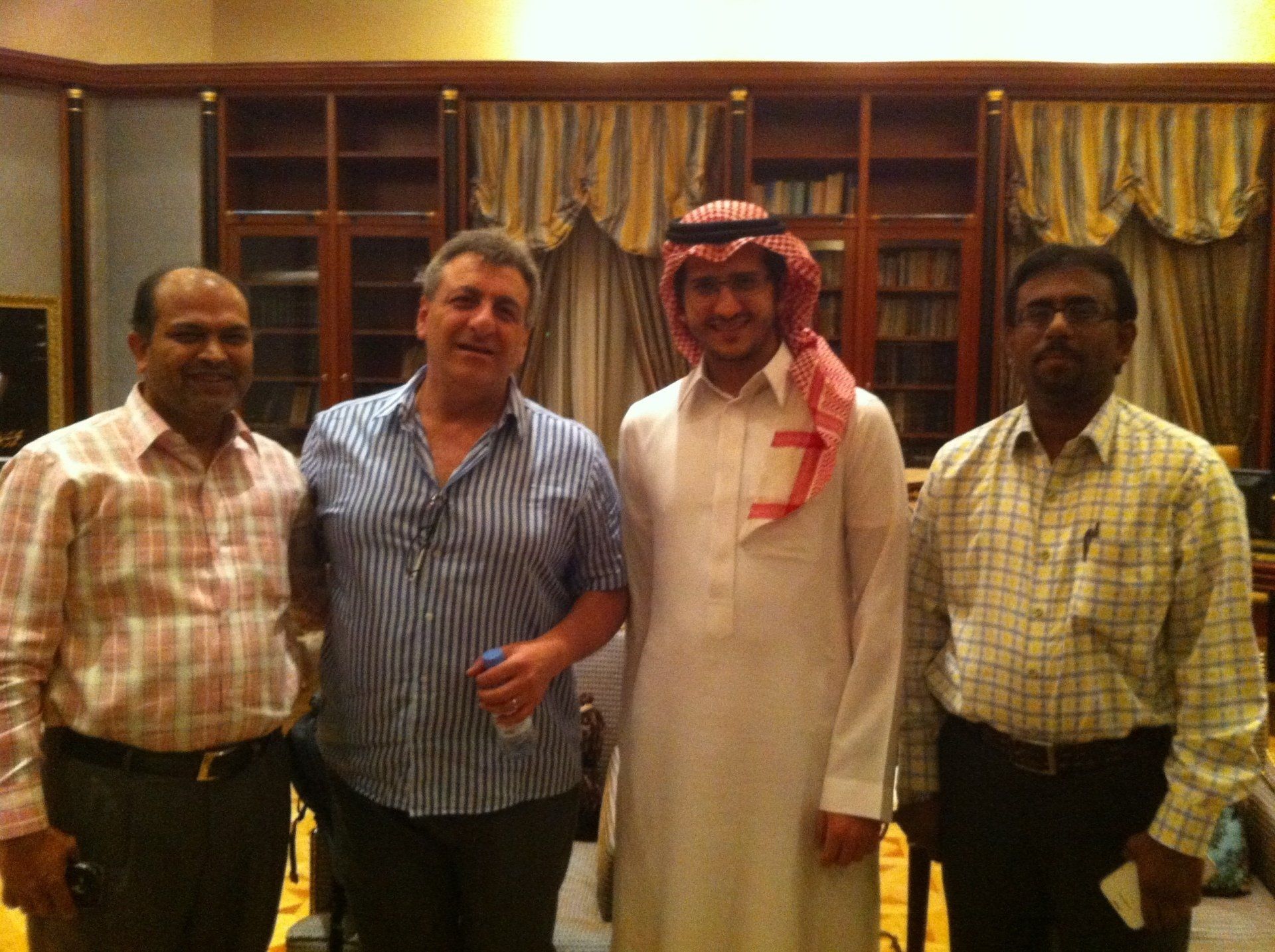 Four people posing together indoors, one in traditional Saudi attire.