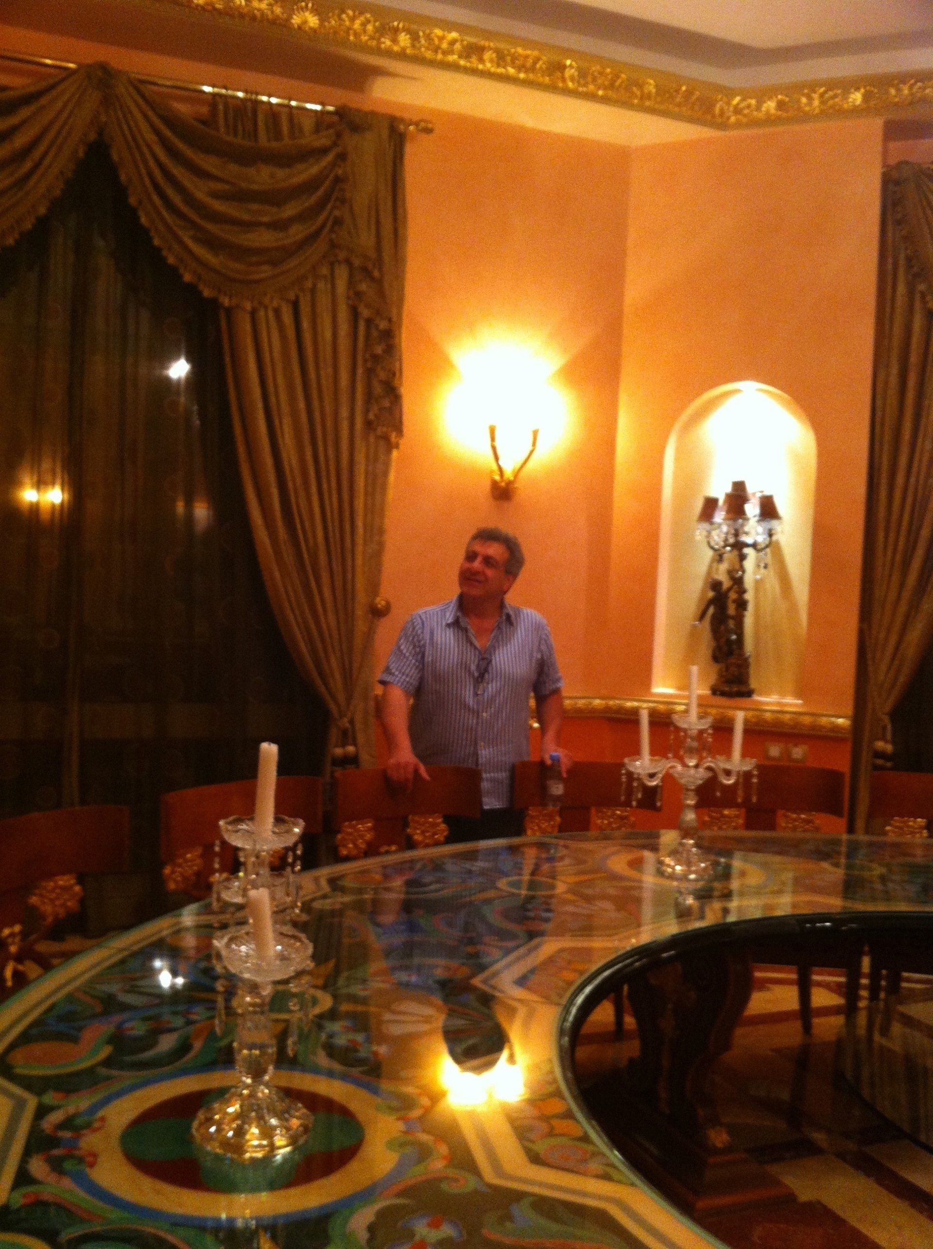 Man stands in ornate dining room with a large table, candles, and a curved window with drapery.