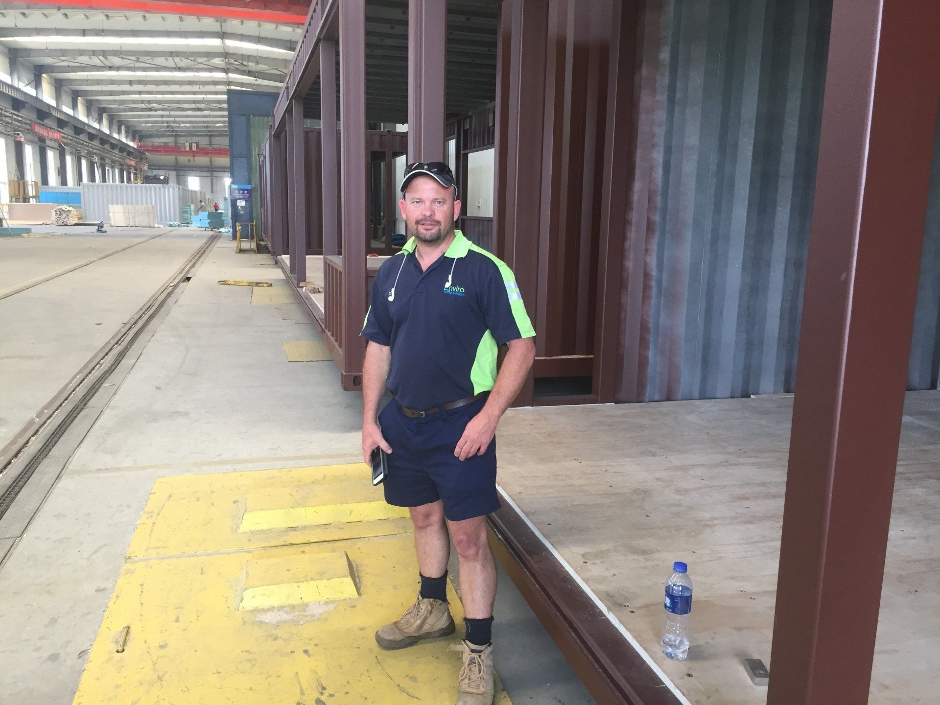 Man in work clothes stands near a large industrial structure inside a factory.