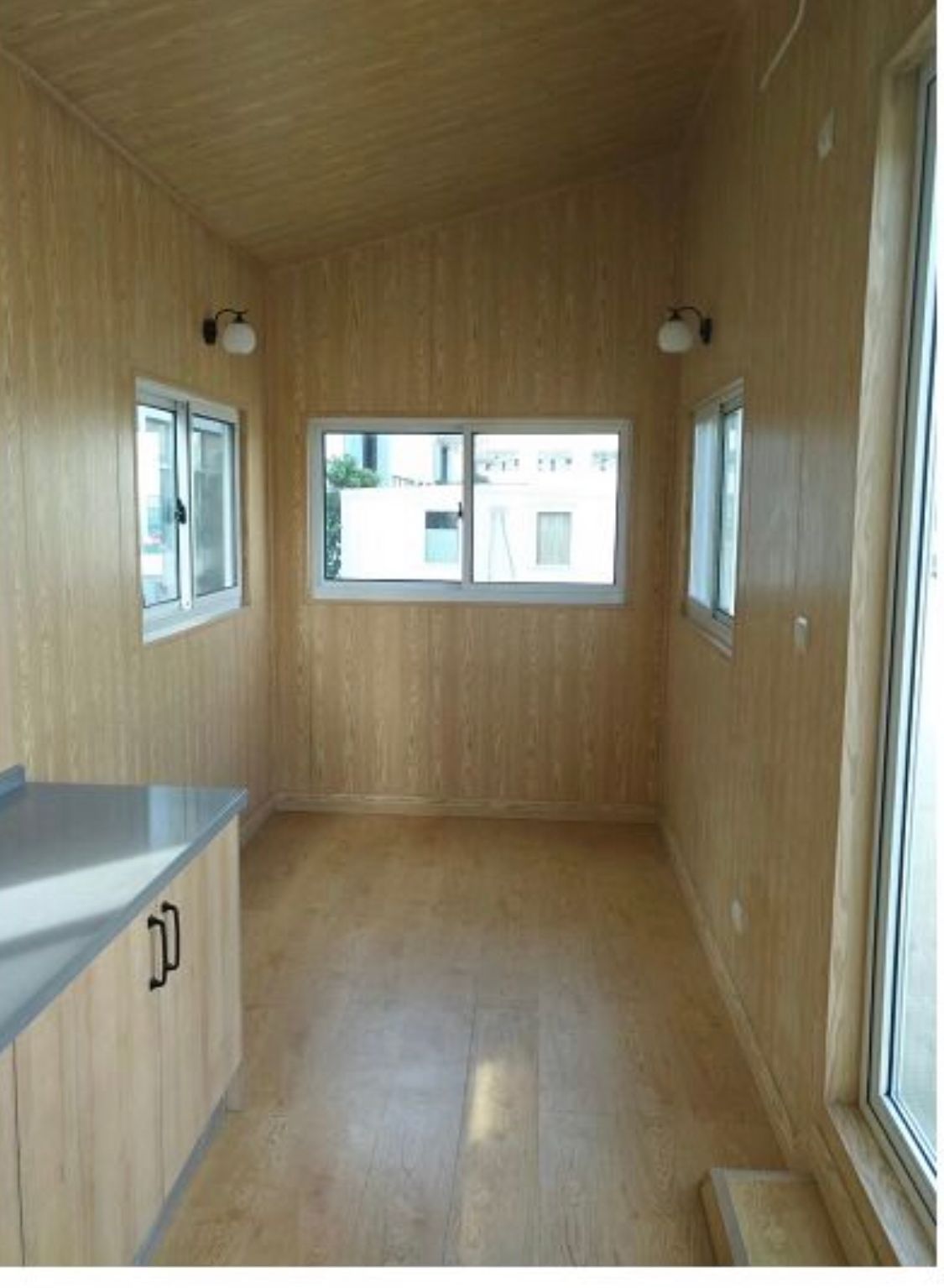 Interior of a small room with wood-paneled walls, multiple windows, and a counter with cabinets.
