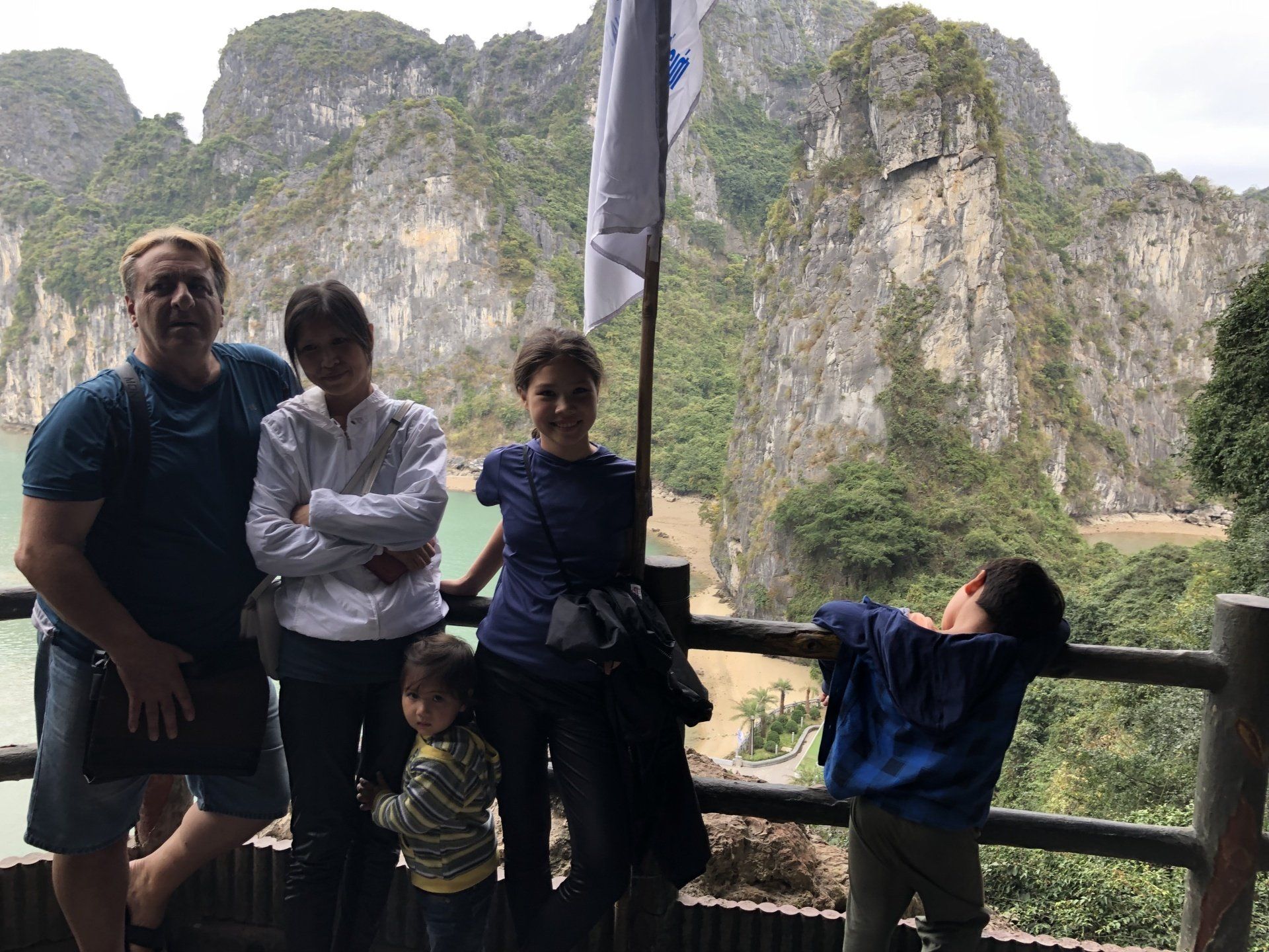 Family posing on a wooden deck with a mountain and water background. Cloudy day.