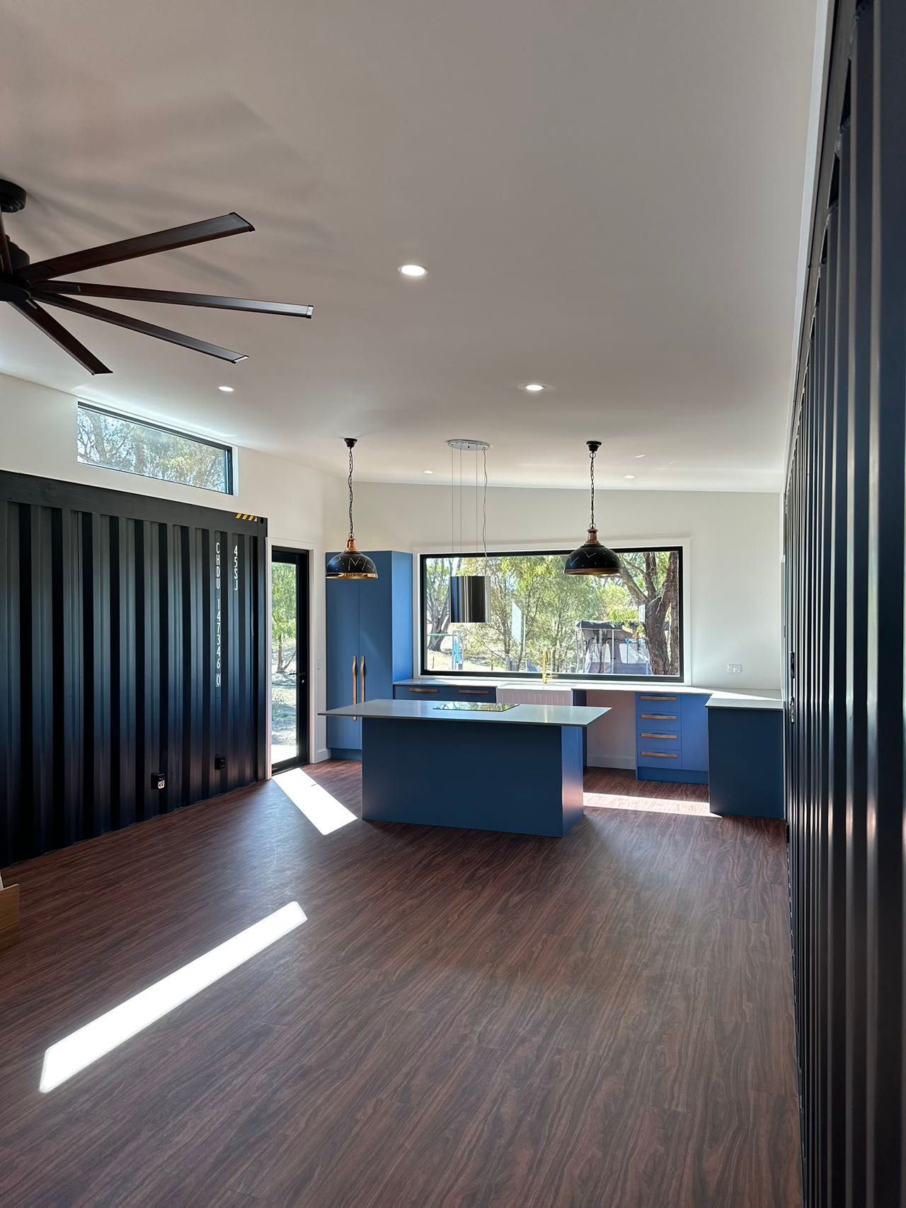 Interior of a blue kitchen with large window overlooking greenery. Two pendant lights hang over the blue island.