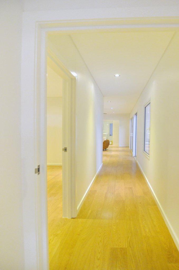 Long hallway with light wood flooring and cream walls, a door on the left and windows on the right.