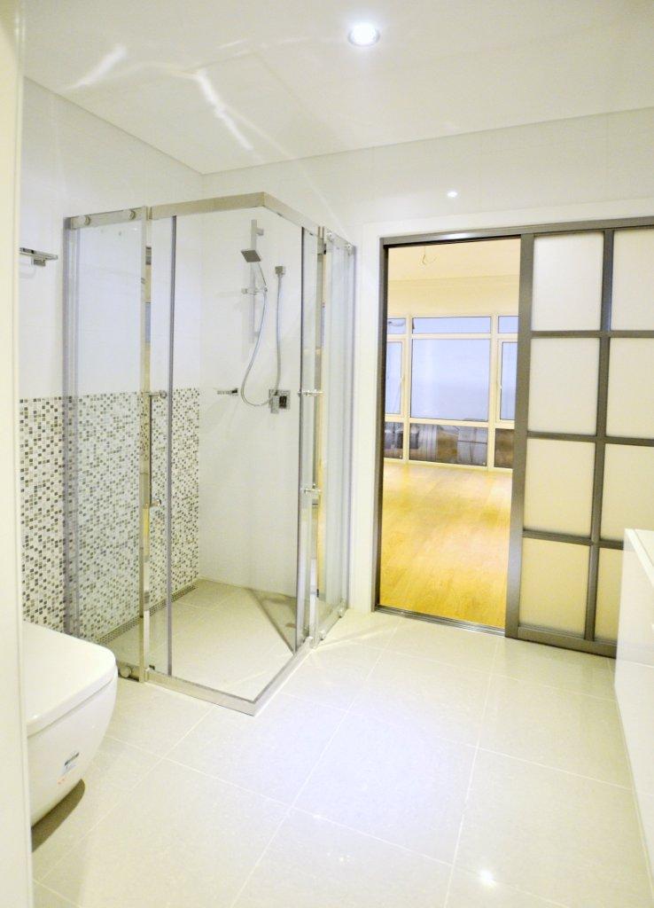 Modern bathroom with glass shower, mosaic tile accent, and sliding door to balcony.