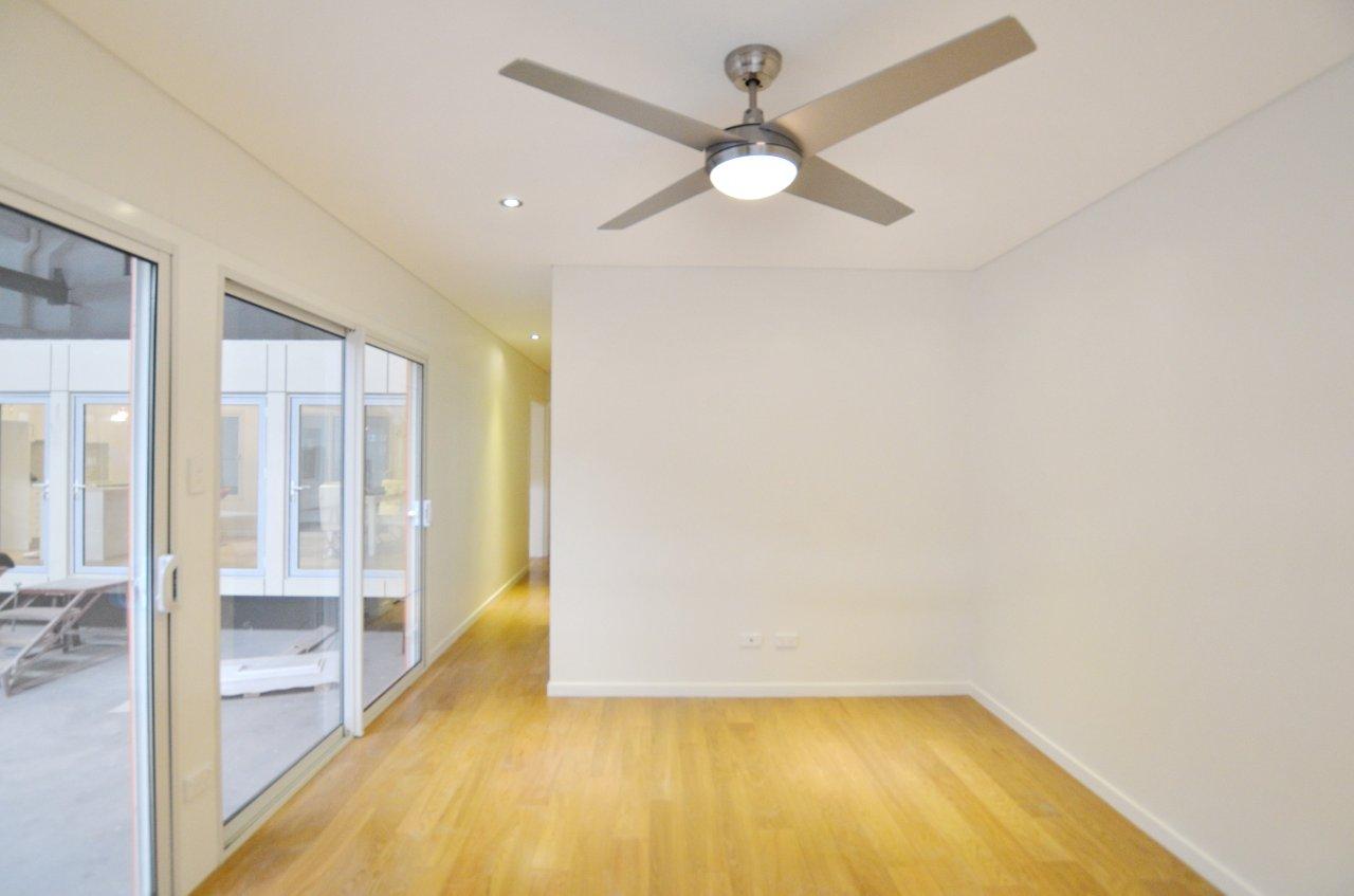 Empty room with wood floor, white walls, and sliding glass doors; a ceiling fan is centered.