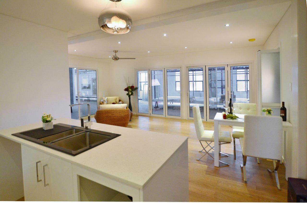 Modern open-plan kitchen and dining area with white cabinets, wooden floor, and large windows.