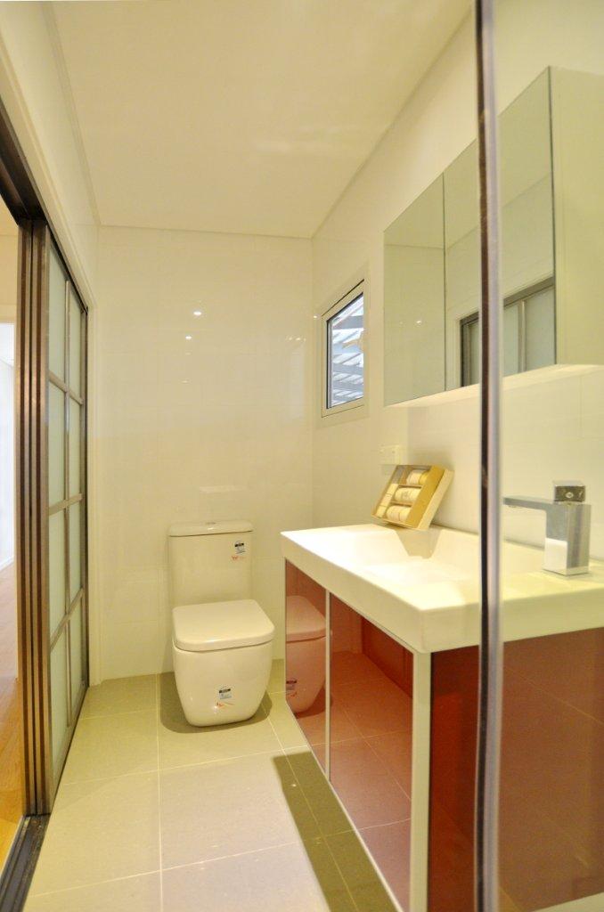 Modern bathroom with a toilet, vanity, and sliding glass door. White walls, red vanity.