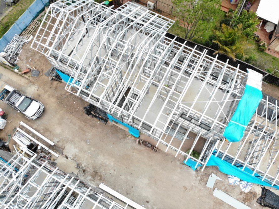 Overhead view of a building under construction, metal frame structure, with turquoise tarps and a parked truck.