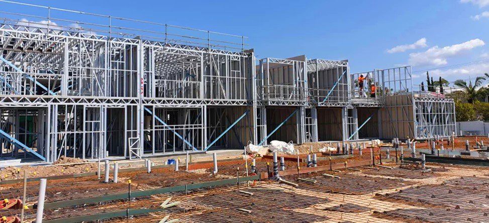 Construction site with metal framing of a two-story building under a blue sky.