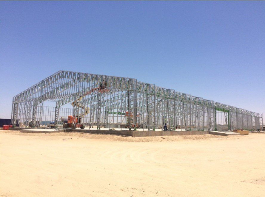 Steel frame of a large building under construction in a desert setting; lift machinery visible.