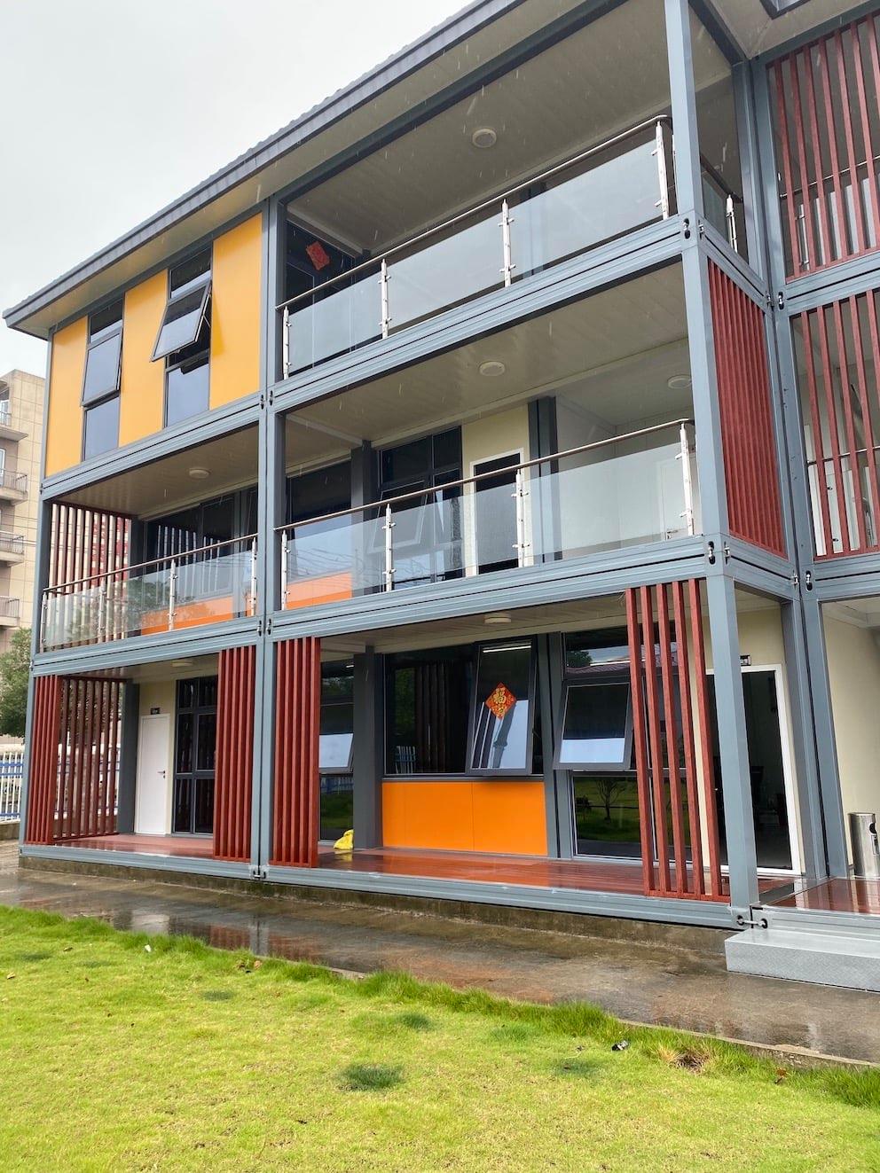 Three-story modern building with orange and brown accents, balconies, and glass railings.