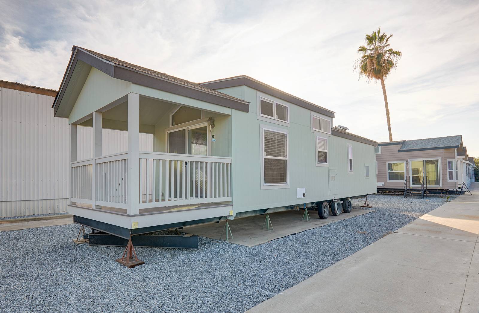 Light green manufactured homes parked on gravel with a palm tree in background.