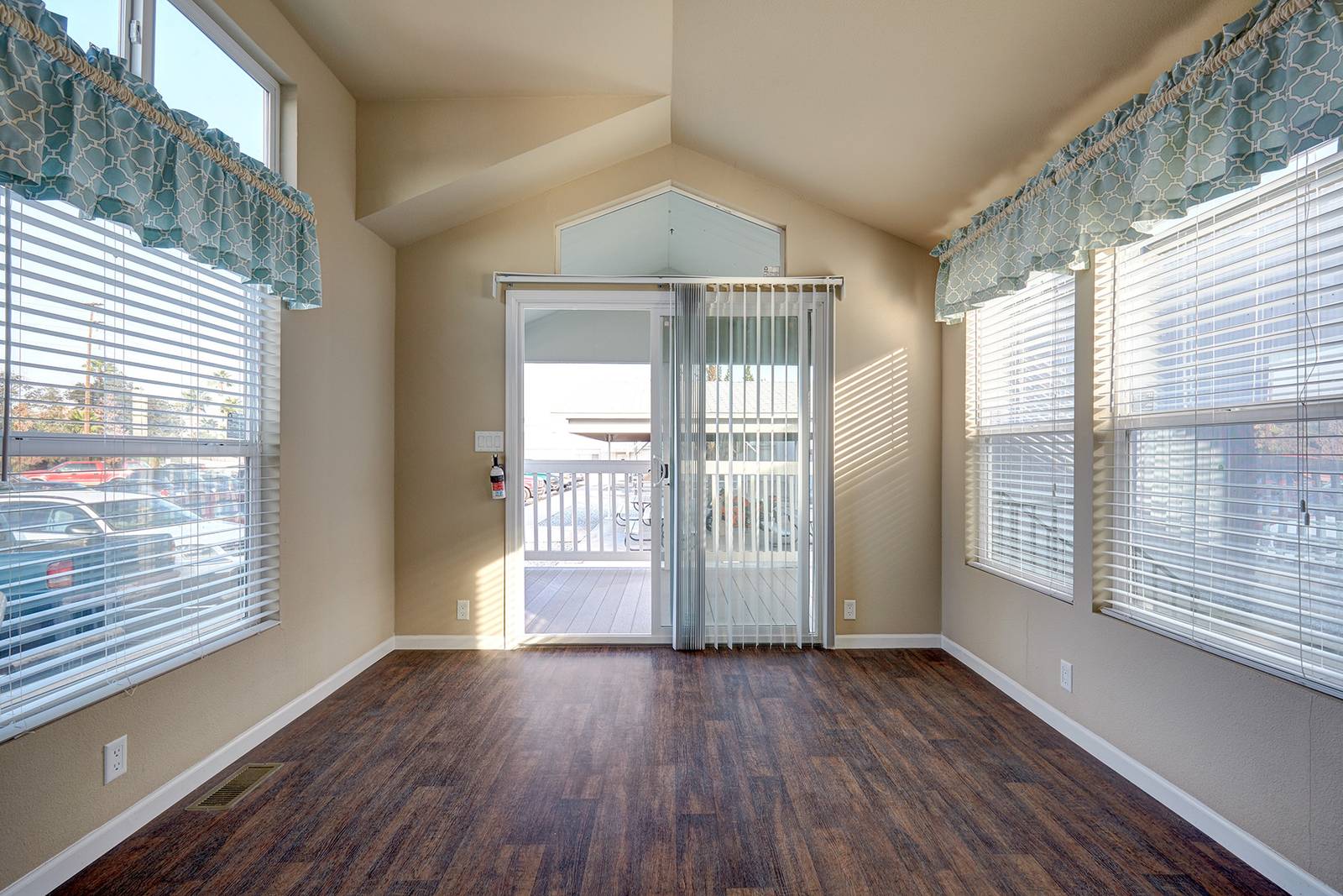 Interior room with windows, sliding glass door to deck, dark wood floor, light beige walls, and blue window valances.