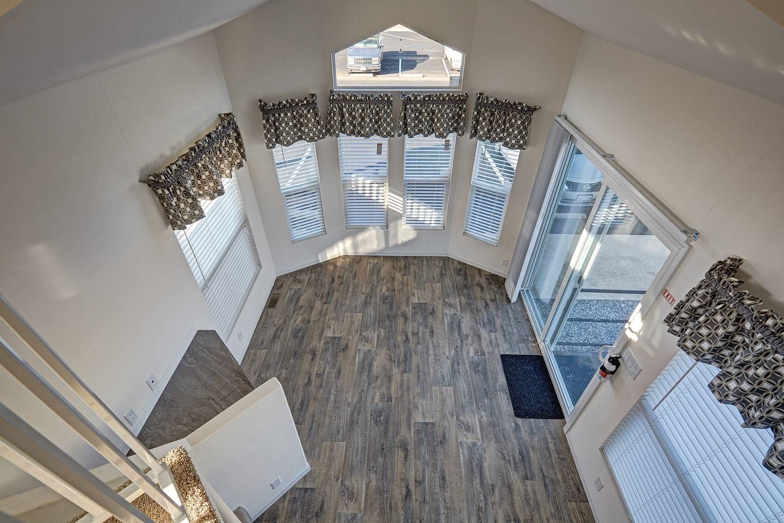 Interior view of a tiny home with windows, a door, and wooden-look flooring. Staircase is visible on the left.
