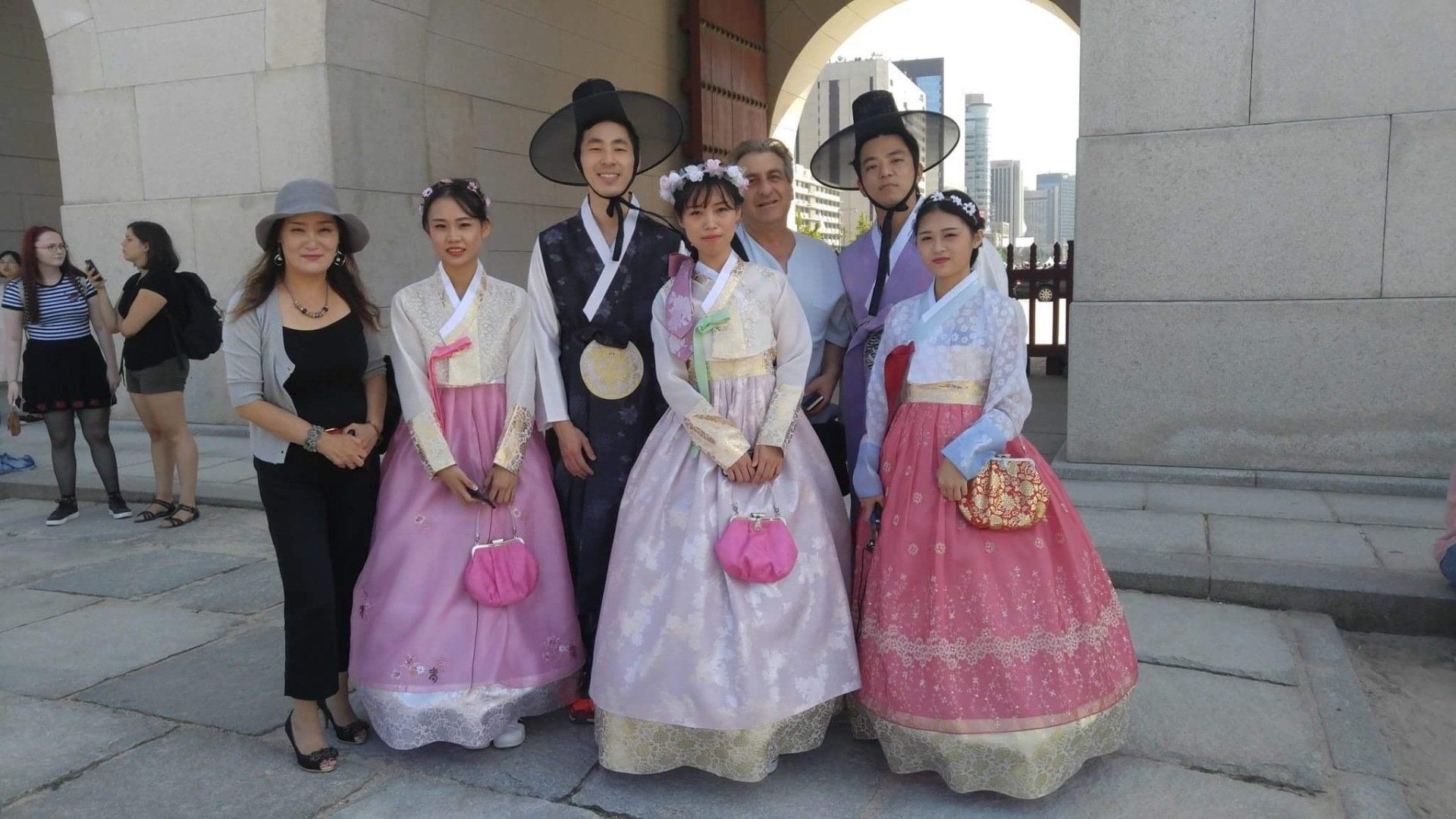 Group of people in traditional Korean hanboks pose at a stone gate in the sunshine.