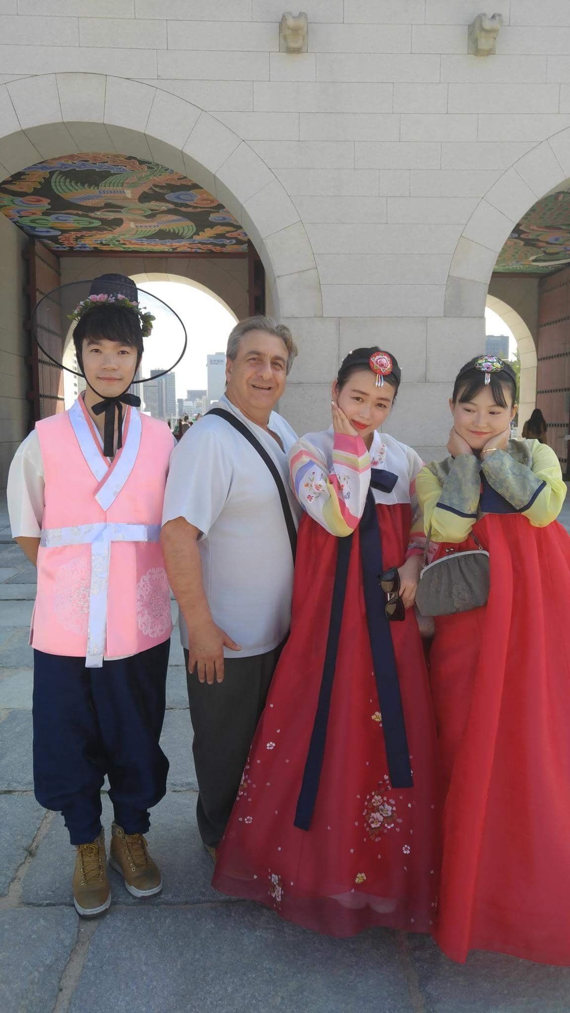 Man poses with three people in Korean traditional clothing near an arched structure.