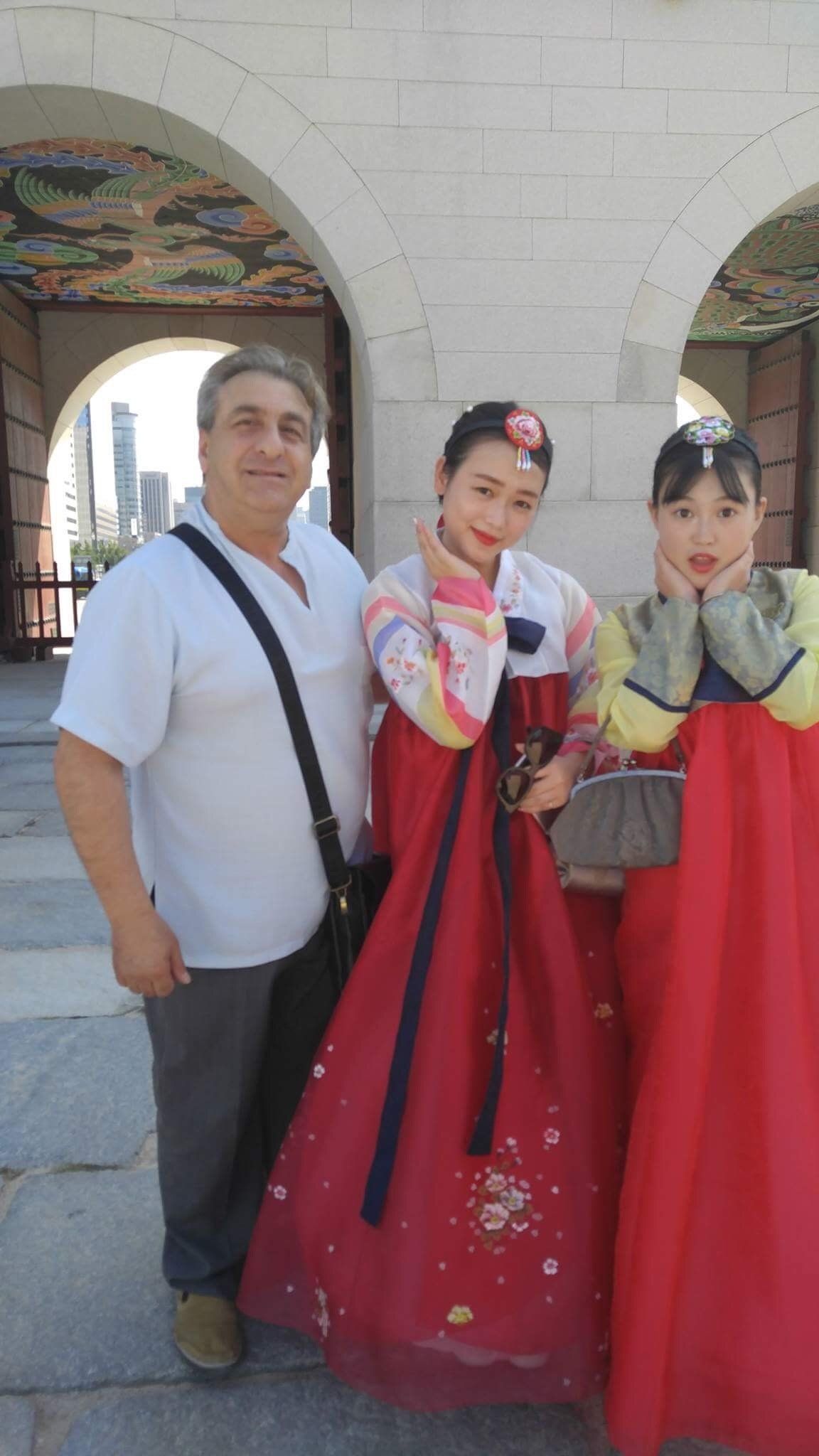 Man poses with two women in traditional Korean hanbok attire, outside a stone archway.