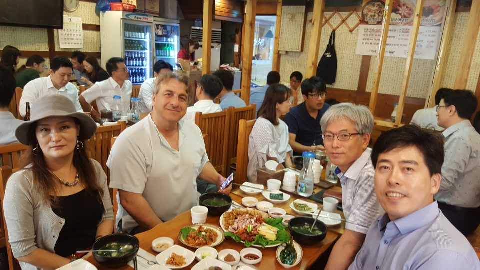People seated at a restaurant table with food, others dining in the background.