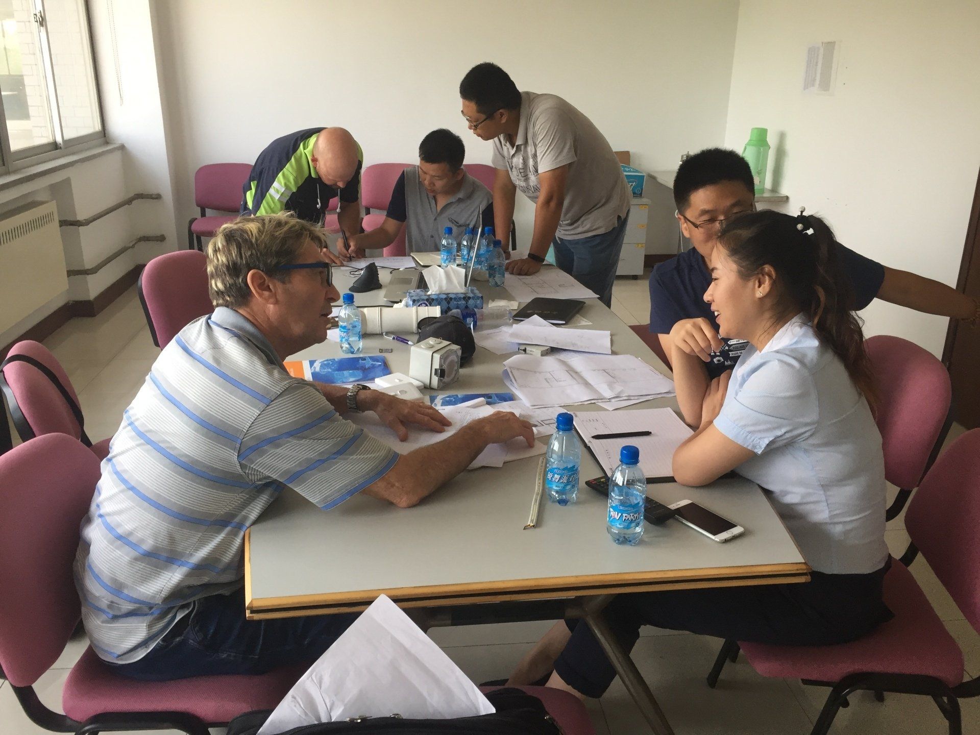 People around a table discussing documents, bottles of water, in an office setting.