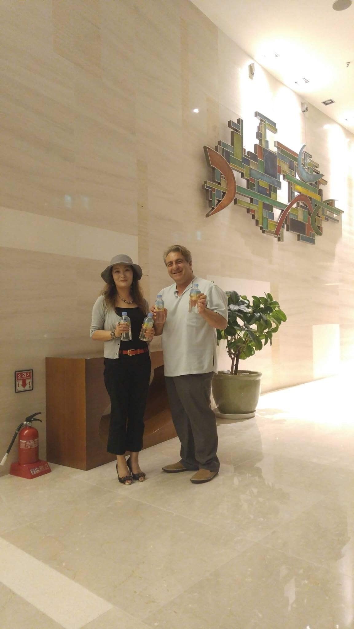 Woman and man holding objects, posing in a well-lit lobby with modern art.