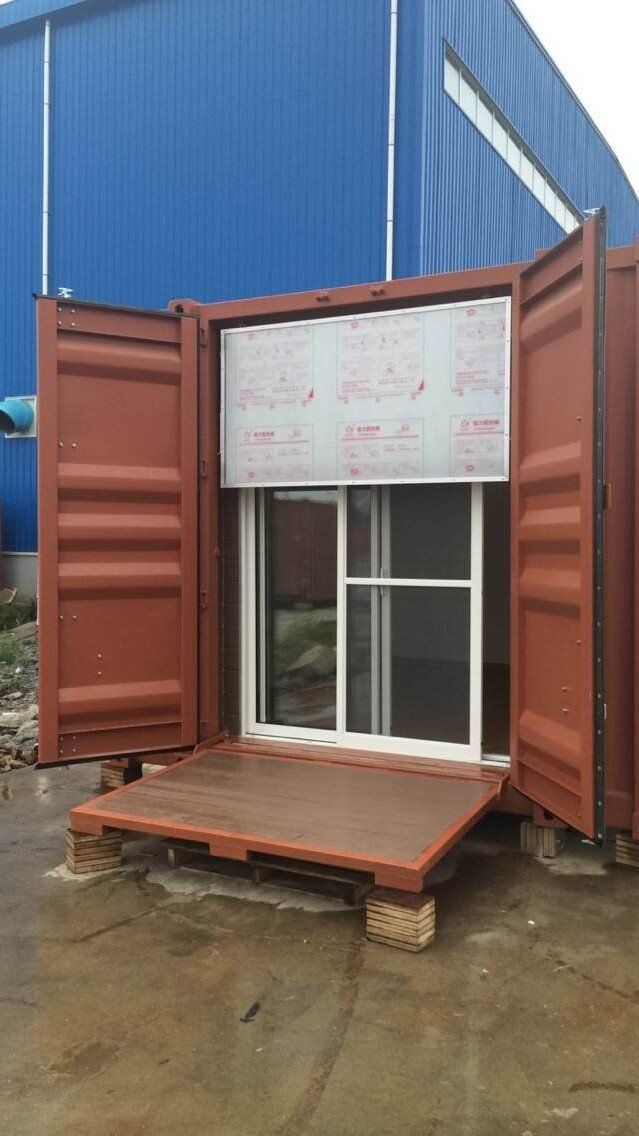 Red shipping container modified into a building, open doors, with a window and small platform.