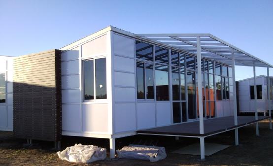White modular building with glass walls, an open deck, and a metal roof.