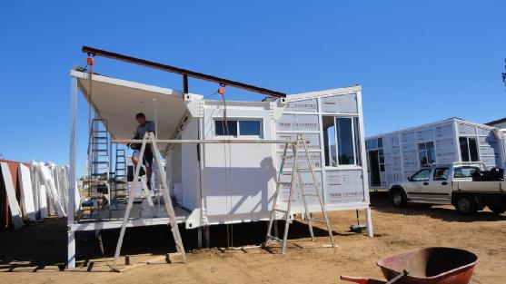 Construction of a white modular home in progress. A person works on the roof under a clear blue sky.