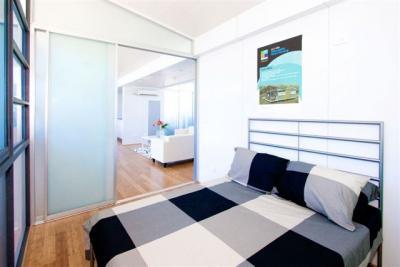 Bedroom with bed, plaid bedding, frosted glass sliding door, and view to a living room.