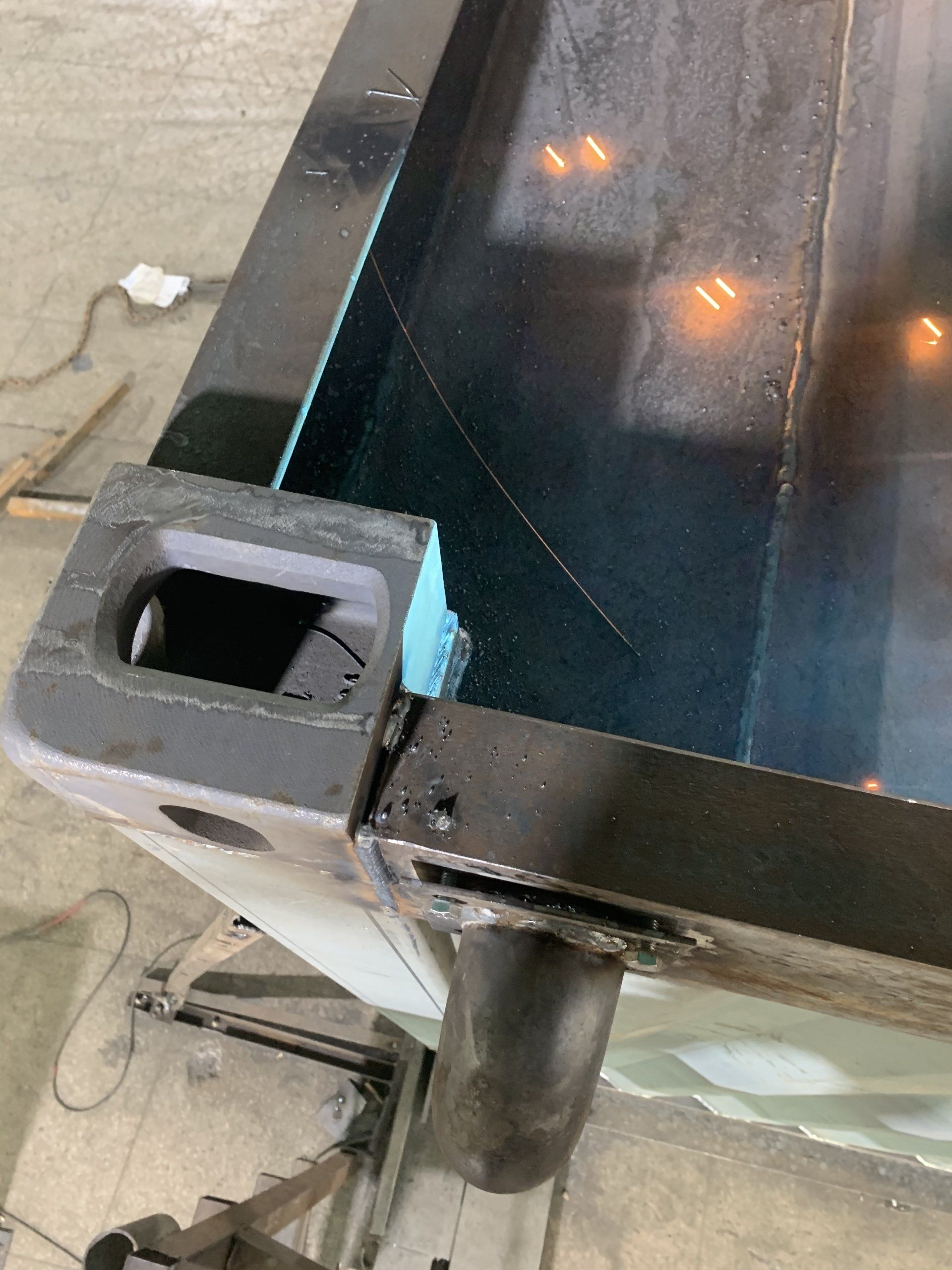 Close-up of a dark metal table corner with a leg. The corner has an opening and is welded together.