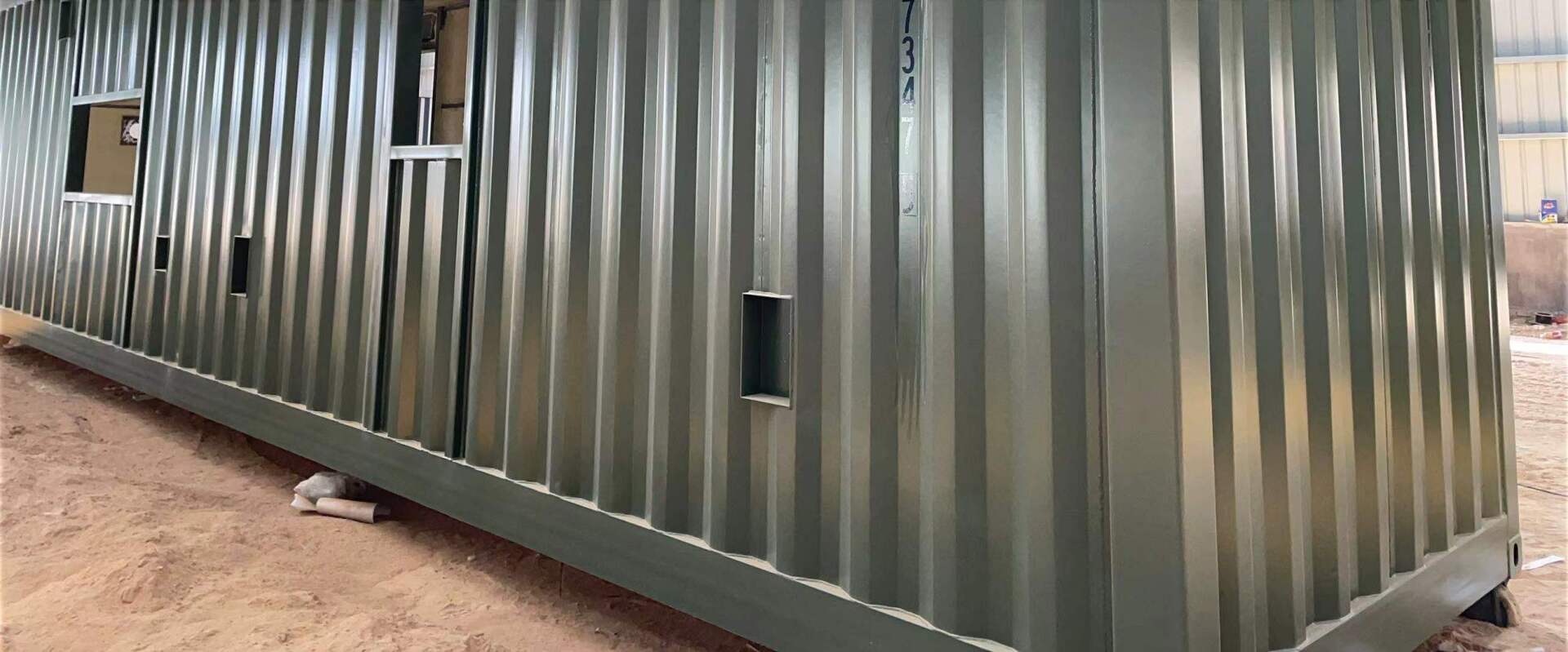 A long, corrugated metal container building, with windows and a door.