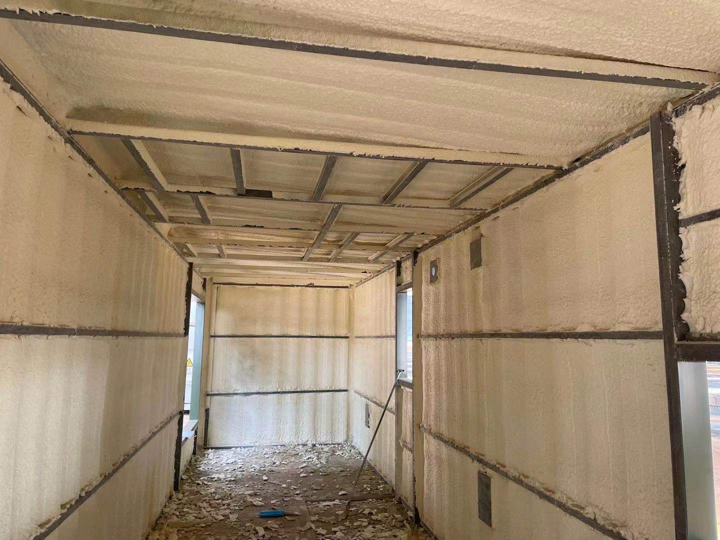 Interior of a structure insulated with light tan spray foam. Metal beams frame walls and ceiling.