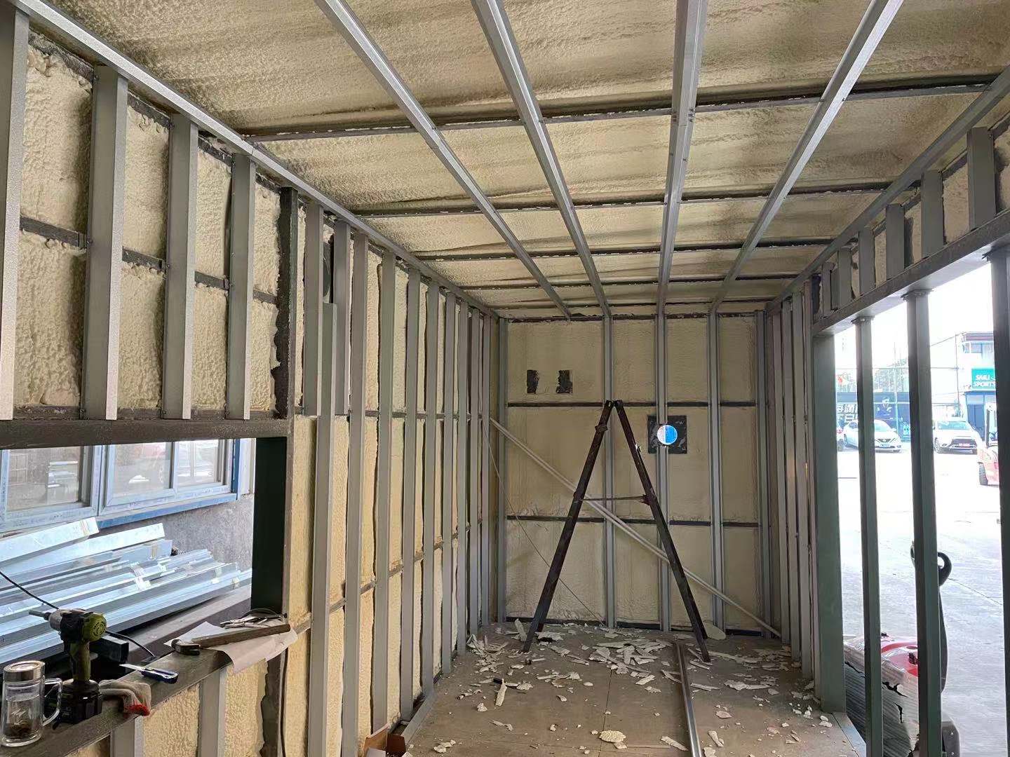 Interior view of a building under construction. Metal framing with spray foam insulation on walls and ceiling.