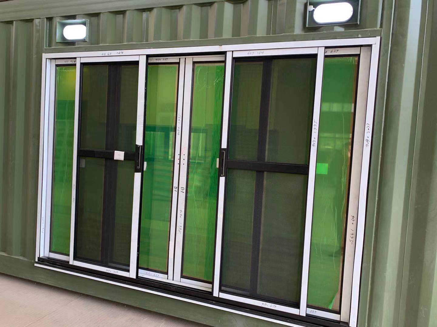 Green tinted sliding glass doors on a green shipping container, with two overhead lights.