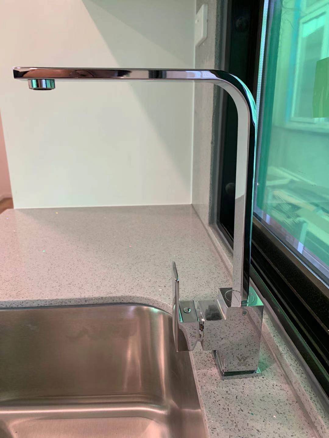 Shiny chrome kitchen faucet over a stainless steel sink, set against a speckled countertop and window.