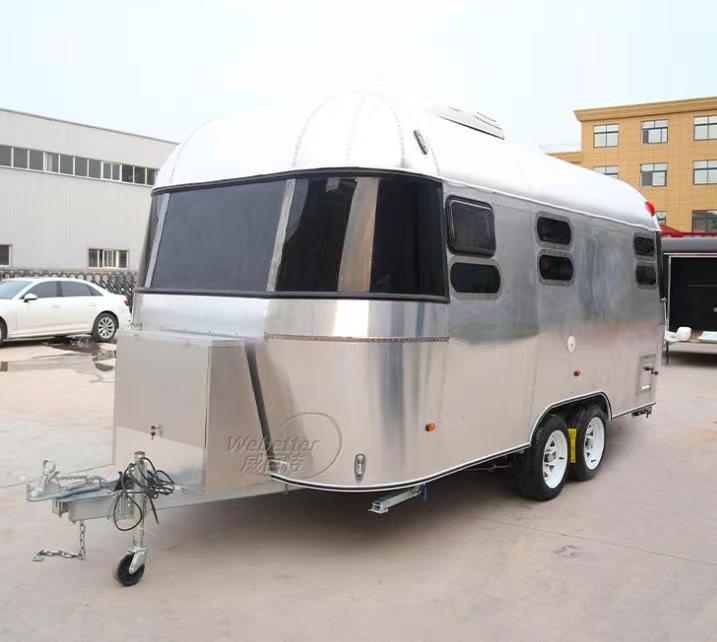 Shiny, silver travel trailer with dark windows and a curved roof, parked outside.