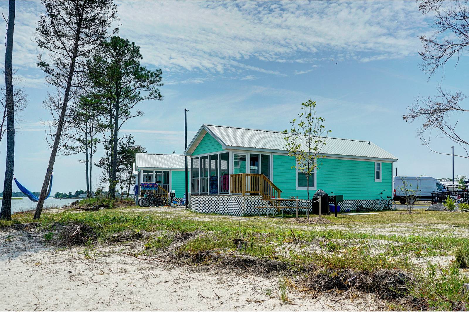 Turquoise beach cottages with white trim and metal roofs, under a partly cloudy sky.