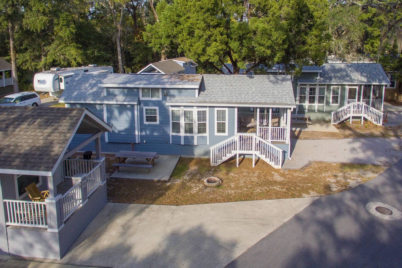 Cottages in a park setting, various shades of blue and gray with white accents. Gray rooftops, green trees in the background.