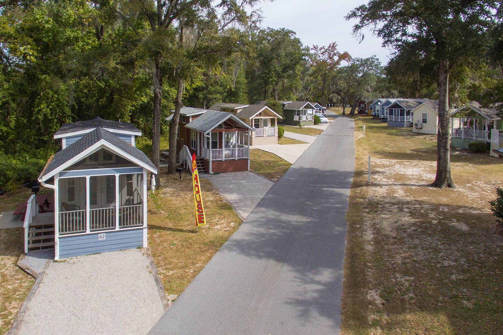 A row of small, colorful cottages with porches line a paved road, set amongst trees.