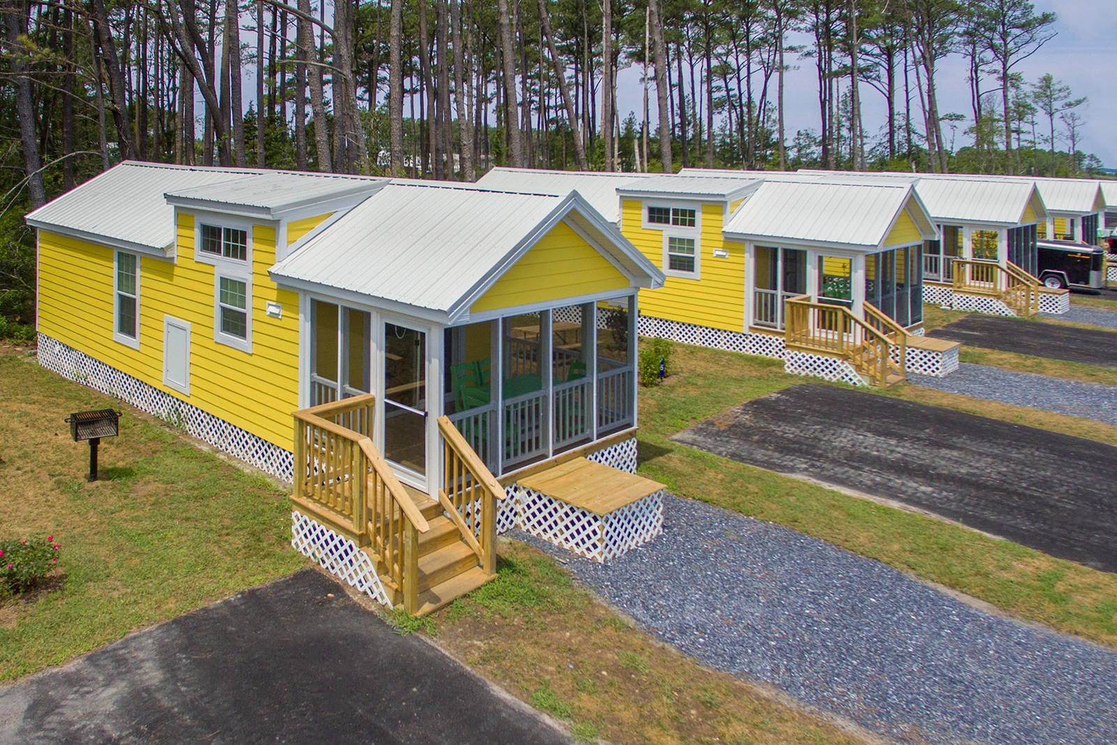 Row of yellow cabins with screened-in porches, white metal roofs, and wooden steps, in a wooded area.