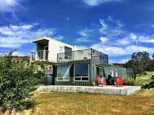 Shipping container home with two levels, windows, and balcony, against a blue sky.