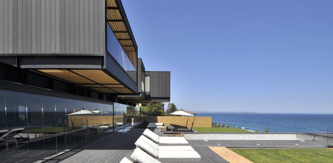 Modern seaside home with dark gray exterior, glass walls, and a view of the ocean.