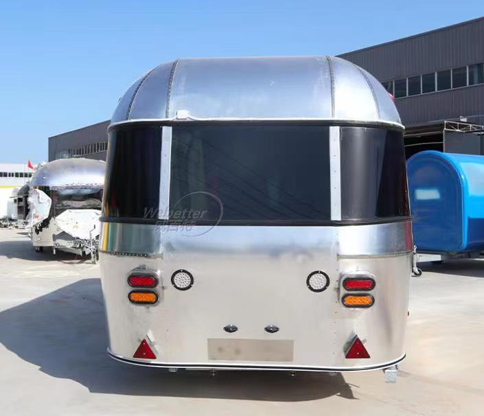 Silver, teardrop-shaped travel trailer with black window, red and orange lights, and small triangular reflectors.