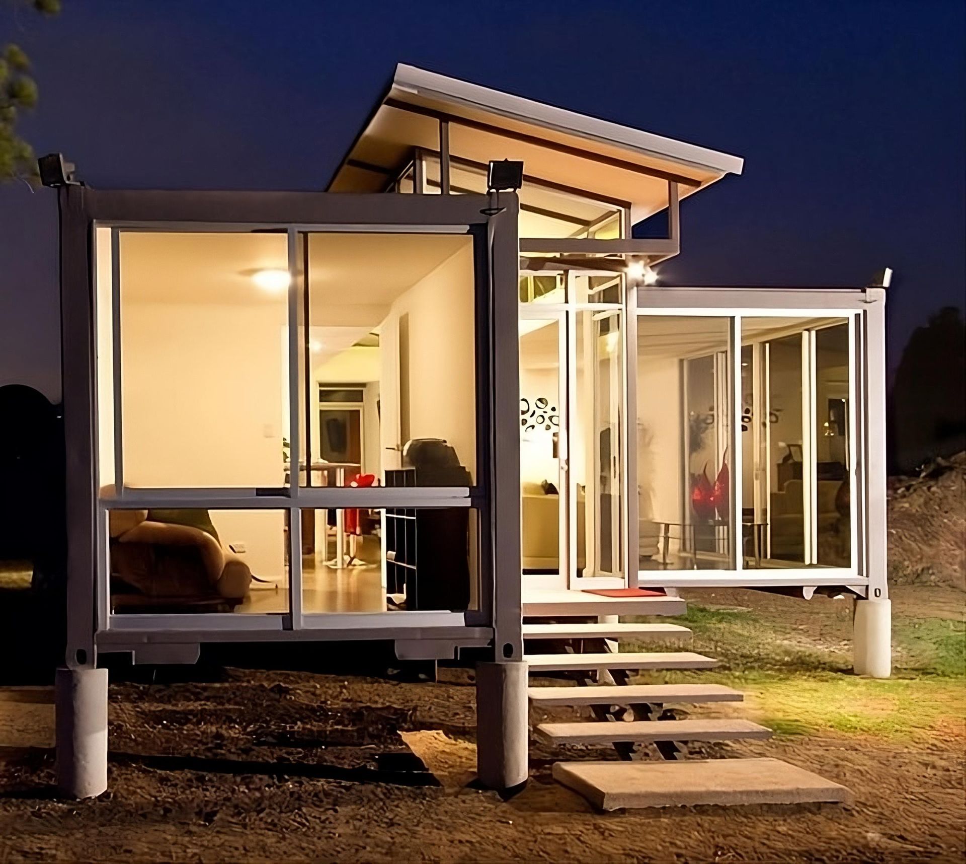 Modern home built from shipping containers at night, with glass walls and elevated entrance.